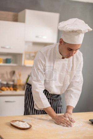 Foto de Profesional maestro chef amasando intensamente en una superficie de harina en las etapas iniciales de la fabricación de pan en una cocina comercial. Mostrando habilidades, técnica, precisión, pasión y arte para la comida. - Imagen libre de derechos