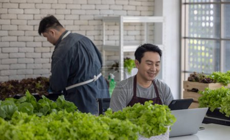 Zwei Gemüseverkäufer, einer hantiert mit einem Laptop und der andere organisiert Grünzeug, demonstrieren eine effiziente Bestandsverwaltung innerhalb eines städtischen Marktes.