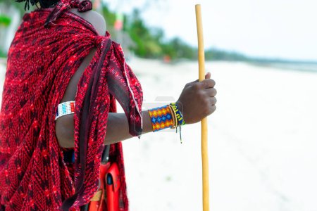 Foto de Maasai, dressed in his traditional exotic clothes, stands on a beach in Zanzibar and enjoys the view of the ocean, creating a contrast between his attire and the beauty of nature - Imagen libre de derechos