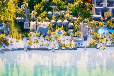 Téléchargez les photos : Top view of a tropical landscape in Zanzibar, Africa, featuring white sandy beaches, blue ocean waves, palm trees, and parasols. The aerial view captures the picturesque scene at sunset, creating the perfect setting for a summer holiday - en image libre de droit