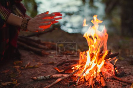 Photo for Close up campfire concept photo. Make fire in forest. Hiking and recreation. Side view photography with woman hands on background. High quality picture for wallpaper, travel blog, magazine, article - Royalty Free Image