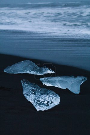 Téléchargez les photos : Gros plan glace claire sur Reynisfjara plage concept photo. La beauté arctique. Photographie vue de face avec ligne de survol en arrière-plan. Image de haute qualité pour papier peint, blog de voyage, magazine, article - en image libre de droit