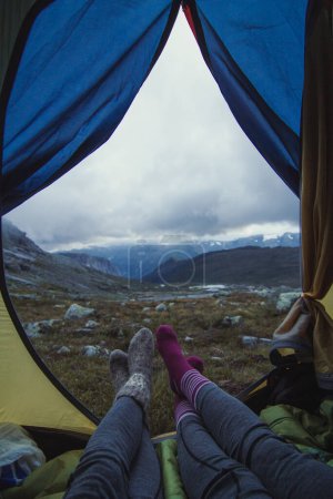 Close up friends in camp at mountain valley concept photo. First view person photography with overcast sky on background. High quality picture for wallpaper, travel blog, magazine, article