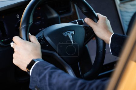 Téléchargez les photos : Lviv, Ukraine - 17 octobre 2022 : Homme d'affaires méconnaissable conduisant sur un nouveau modèle de voiture Tesla le long des rues, à l'intérieur de la conduite de la voiture Tesla à l'aide d'un moniteur avant. Voiture de conduite masculine utilisant le pilote automatique - en image libre de droit