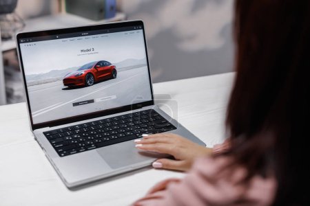 Photo for CALIFORNIA, USA - NOVEMBER 14, 2022: Middle eastern woman using laptop buying electric car online on tesla website. Shopping for a Tesla car browsing different models with the intent to purchase. - Royalty Free Image