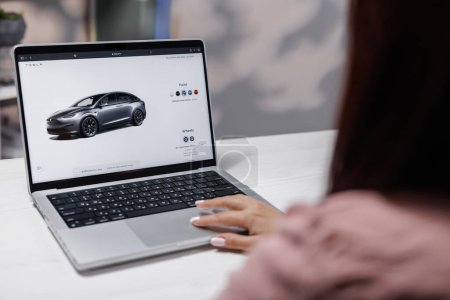 Photo for CALIFORNIA, USA - NOVEMBER 14, 2022: Tesla website, buying a car online. Woman using laptop computer ordering Tesla model X Plaid Choice colors and full self-driving autopilot. - Royalty Free Image
