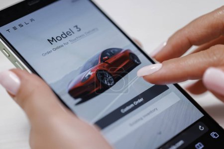 Photo for CALIFORNIA, USA - NOVEMBER 14, 2022: Woman using smartphone application. Tesla website, buying a car online. Female touches smart phone close-up. Browsing the different tesla models on their website. - Royalty Free Image