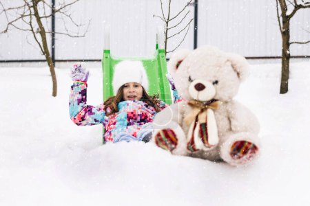Téléchargez les photos : Cute toddler girl playing with teddy bear in winter park. Winter portrait of little caucasian child girl. Outdoor winter activities for kids. - en image libre de droit