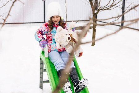 Téléchargez les photos : Child with toy teddy bear sits on a sled. Winter vacantion. Christmas celebration and winter holidays. Winter fun and outdoor activities with kids. - en image libre de droit