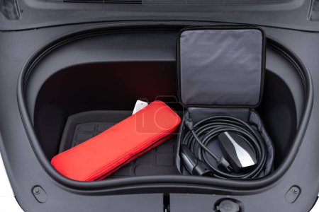 Electric car charger in car trunk. Front trunk with charging cables. Modern interior. Portable in-cable charging box for electric car charging lying in car trunk