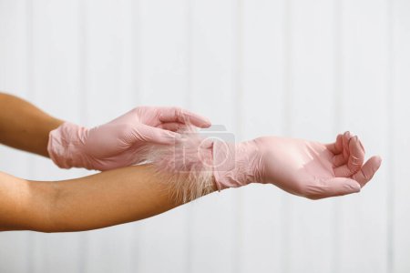 Feder zu weiblicher Hand auf weißem Hintergrund. Konzept der Leichtigkeit und Sauberkeit. Hautpflege für die Hand. Frauenhände mit weicher Feder. Körperpflege