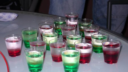 Téléchargez les photos : Verres de tir sur la vieille table vert vodka rouge gueule de bois. Photo de haute qualité - en image libre de droit