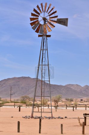 Téléchargez les photos : Pompe à vent en Namibie désert Afrique Ciel bleu Montagnes Énergie éolienne. Photo de haute qualité - en image libre de droit
