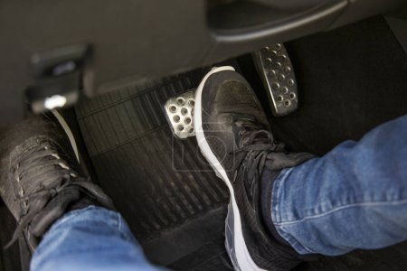 Photo for Man's feet in black sneakers on the floor in a car pushing down the brake pedal, carefully driving car, waiting on the traffic light concept - Royalty Free Image