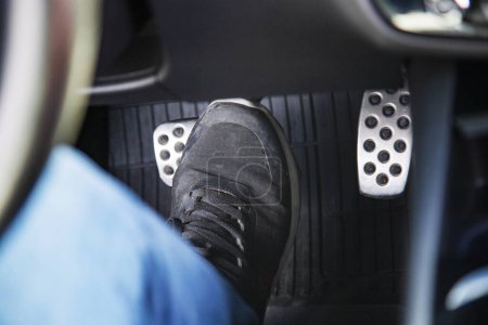 man's feet in black sneakers on the floor in a car pushing down the brake pedal, carefully driving car, waiting on the traffic light concept