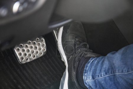 Paar schwarzer Turnschuhe auf dem Boden in einem Auto, das auf das Gaspedal drückt, vorsichtig fahrendes Auto-Konzept