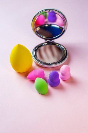 Mélangeur coloré maquillage éponges mélange jeu de bouffées et miroir en forme ronde sur un fond rose avec espace de copie. concept de beauté photo verticale