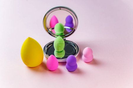 Colorful blender makeup sponges blending puff set and round shaped mirror on a pink background with copy space. beauty concept