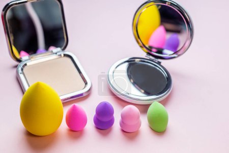 Mélangeur coloré maquillage éponges mélange jeu de bouffées et miroir en forme ronde sur un fond rose avec espace de copie. concept de beauté