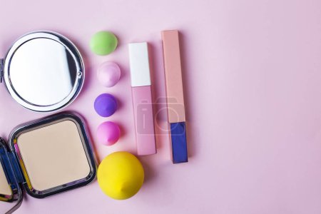 Flat lay composition with cosmetics and makeup products on pink background. Colorful blender makeup sponges blending puff set and round shaped mirror