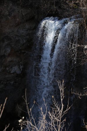 Foto de Cascada en la naturaleza entre rocas, agua blanca que fluye y ramas en el lado de la foto - Imagen libre de derechos