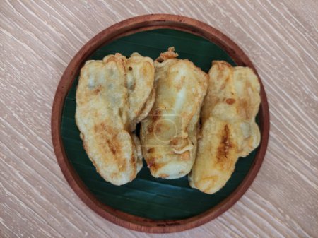 Foto de Buñuelos de plátano o "Pisang Goreng", plátano frito con harina cubierta, servido en placa de madera sobre fondo texturizado de madera. Imagen de enfoque selectivo. - Imagen libre de derechos