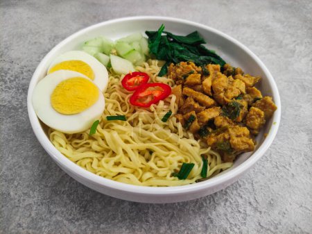 Photo for Mie Ayam, an Indonesian street food. Noodles completed with chicken cubes, egg sliced and vegetables served in a white bowl. Selective focus - Royalty Free Image