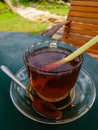Foto de Enjoying a glass cup of hot aromatic tea (with lemon grass) in the backyard, bokeh background, selective focus image - Imagen libre de derechos