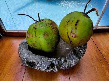 Foto de Redondo de coco verde joven en un plato de piedra en la mesa de madera con fondo de piscina. Imagen de enfoque selectivo - Imagen libre de derechos