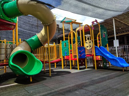 Foto de Malang - Indonesia, 21 de enero de 2023: Moderno parque infantil al aire libre. Tobogán de tubo con estera de goma en la arena del jardín de infantes. No hay gente. - Imagen libre de derechos