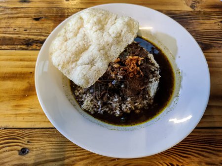 Foto de Rawon, sopa de ternera indonesia con caldo negro, originaria de Surabaya Java Oriental. Se sirve en plato con arroz y galleta - Imagen libre de derechos
