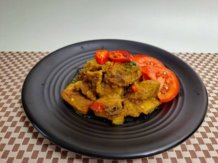 Photo for Tengkleng, indonesian curry with beef or lamb bones as the main ingredients, similar with rica. Served on black plate - Royalty Free Image