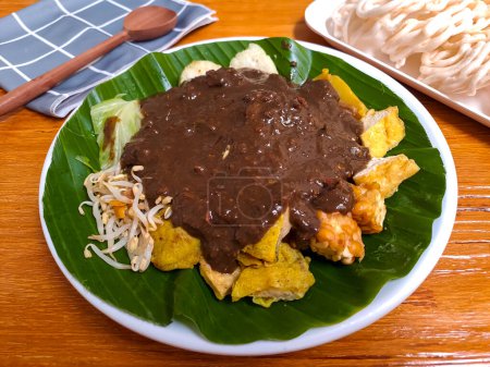 Foto de Rujak Cingur, uno de ensalada indonesia de java oriental que mezcla de varios tipos de verduras, tempeh y nariz de vaca con salsa de maní. Servido en un plato contra mesa de madera, enfoque selectivo - Imagen libre de derechos
