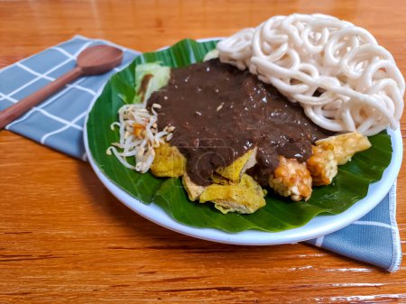 Foto de Rujak Cingur, uno de ensalada indonesia de java oriental que mezcla de varios tipos de verduras, tempeh y nariz de vaca con salsa de maní. Servido en un plato contra mesa de madera, enfoque selectivo - Imagen libre de derechos