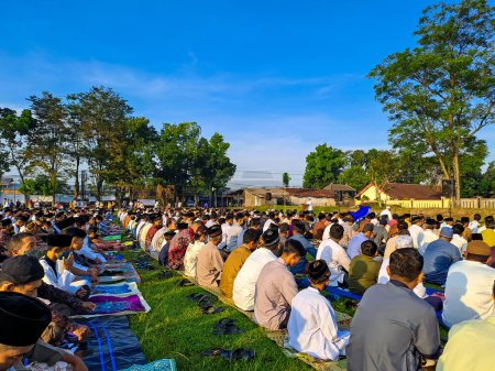 Foto de La gente se está reuniendo en el campo para realizar la Oración del Eid con el cielo azul claro como fondo. Yogyakarta, Indonesia, 21 de abril de 2023. - Imagen libre de derechos