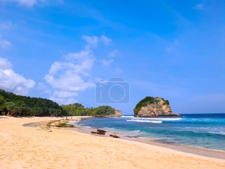 Photo for View of beautiful beach with white sand, rocks, green foliages and calm waves under clear blue sky. Summer vacation concept. Ngudel Beach, Malang, Indonesia - Royalty Free Image