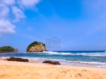 Photo for View of beautiful beach with white sand, rocks, green foliages and calm waves under clear blue sky. Summer vacation concept. Ngudel Beach, Malang, Indonesia - Royalty Free Image