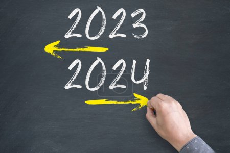 Téléchargez les photos : Gros plan de la main humaine dessin vieille année 2023 et Nouvel An 2024 avec flèche sur fond tableau noir - en image libre de droit