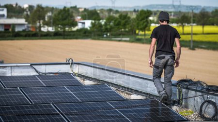 Foto de Male team engineers installing stand-alone solar photovoltaic panel system. Electricians mounting blue solar module on roof of modern house. Alternative energy concept - Imagen libre de derechos