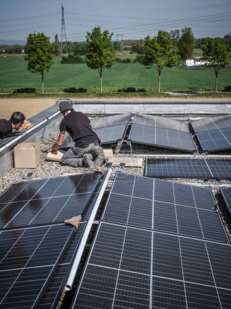 Foto de Male team engineers installing stand-alone solar photovoltaic panel system. Electricians mounting blue solar module on roof of company roof. Alternative energy concept - Imagen libre de derechos