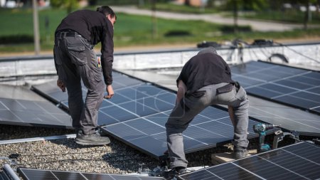 Foto de Male team engineers installing stand-alone solar photovoltaic panel system. Electricians mounting blue solar module on roof of company. Alternative energy concept - Imagen libre de derechos