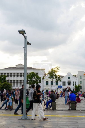 Foto de Felices turistas disfrutando del ambiente nocturno, sentados con amigos y familiares en el patio delantero del Museo Fatahillah, que representa la arquitectura colonial holandesa en la zona turística de Kota Tua, Yakarta del Norte, el 23 de enero de 2023. - Imagen libre de derechos