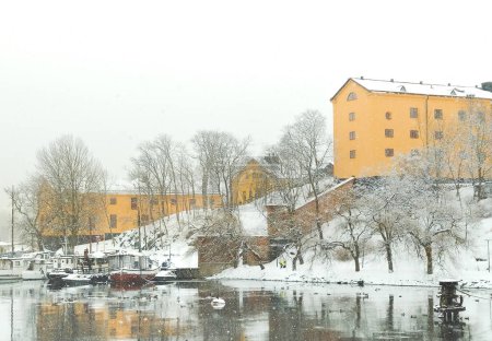 Téléchargez les photos : Bâtiments en pierre jaune de style scandinave avec neige blanche au sol sur Skeppsholmen, Stockholm, Suède au bord de l'eau avec un petit port de plaisance lors de fortes chutes de neige en hiver - en image libre de droit