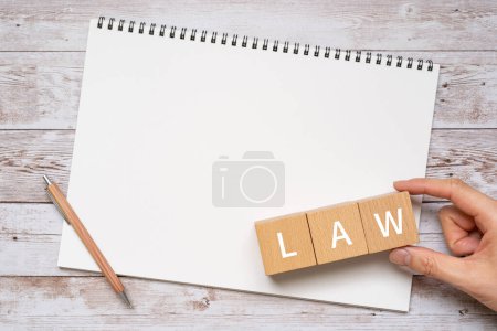 Téléchargez les photos : Blocs en bois avec "LAW" texte de concept, un stylo, un carnet, et une main. - en image libre de droit