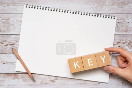 Wooden blocks with "KEY" text of concept, a pen, and a notebook.