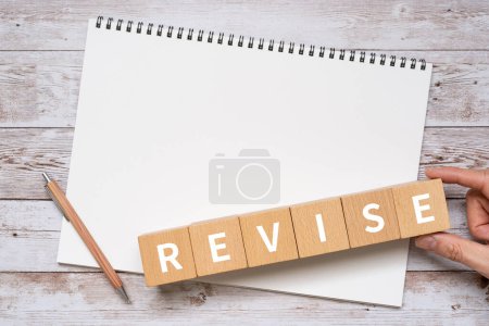 Foto de Bloques de madera con "REVISAR" el texto del concepto, un bolígrafo y un cuaderno. - Imagen libre de derechos
