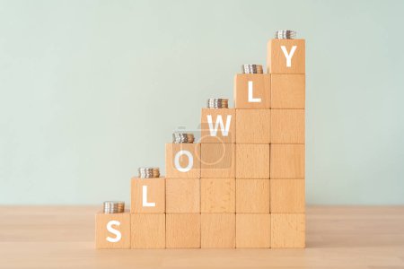 Wooden blocks with "SLOWLY" text of concept and coins.
