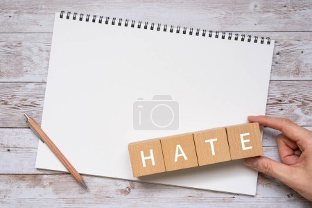 Foto de Bloques de madera con texto de concepto "HATE", un bolígrafo, un cuaderno y una mano. - Imagen libre de derechos