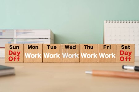 Holzblöcke mit Konzepttext für den Arbeitstag, Stifte, Notizbücher und Bücher.