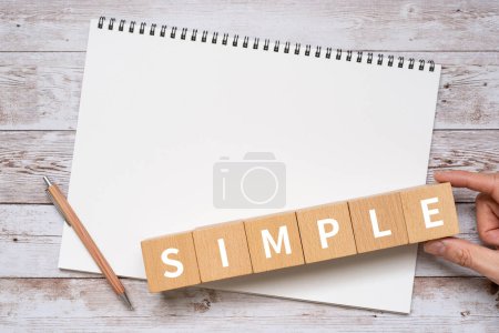 Bloques de madera con texto "SIMPLE" de concepto, un bolígrafo y un cuaderno.